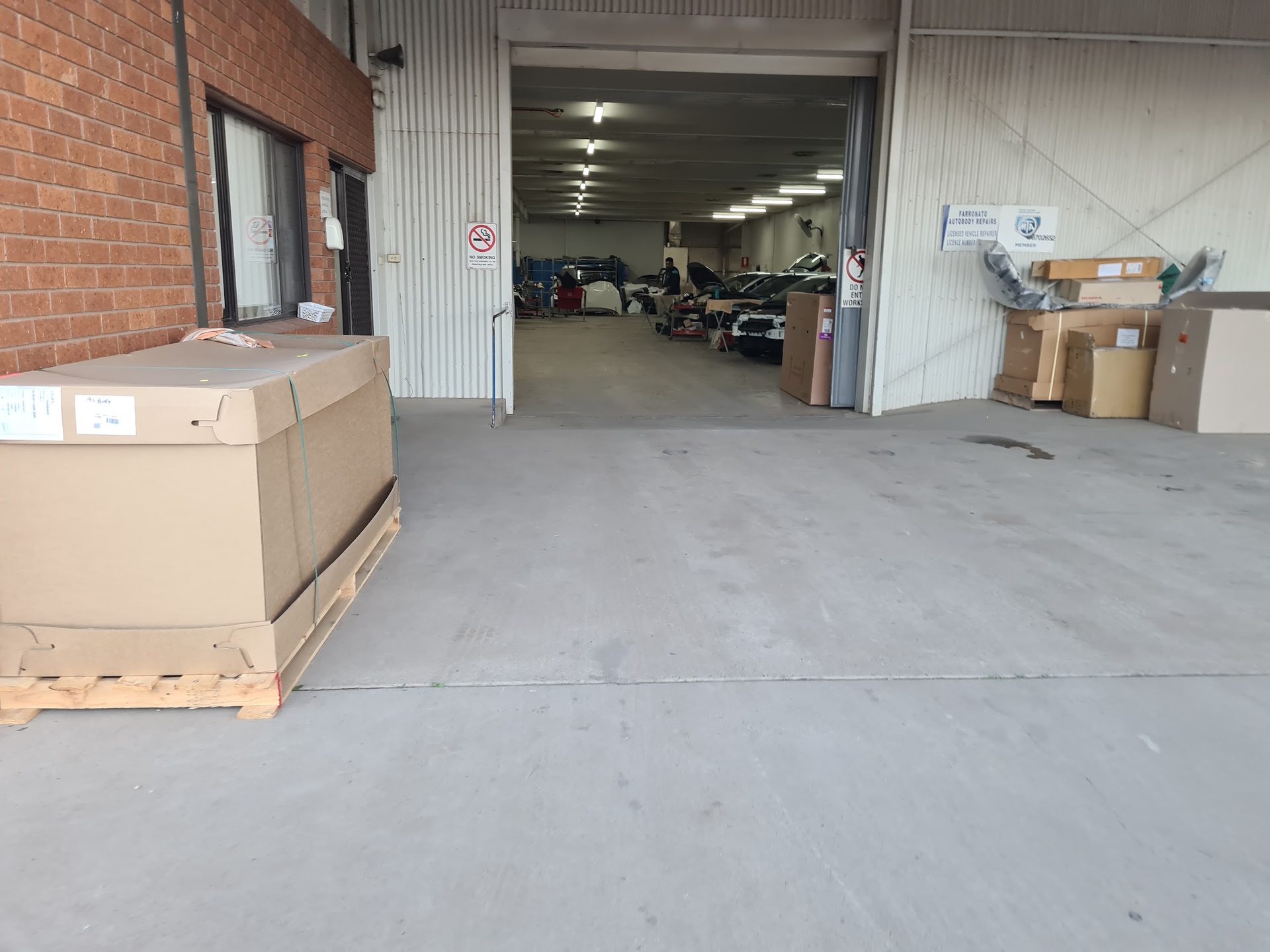Inside the Farronato Autobody Repairs workshop, with cars in the bays and the licence and MTA plaques on the wall